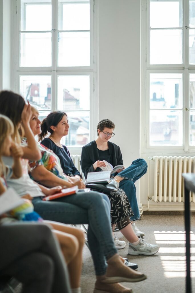 People seated together in a bright room at a recovery support group meeting, holding literature and listening